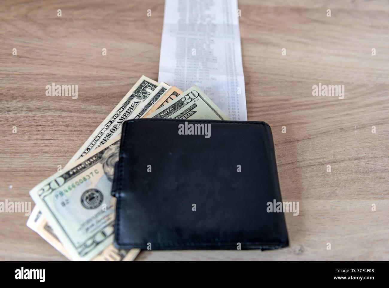Un supermercato fino alla ricevuta su un tavolo con una pila di banconote da dollari americani e una borsa in cima. Un concetto del costo della vita negli Stati Uniti. Foto Stock