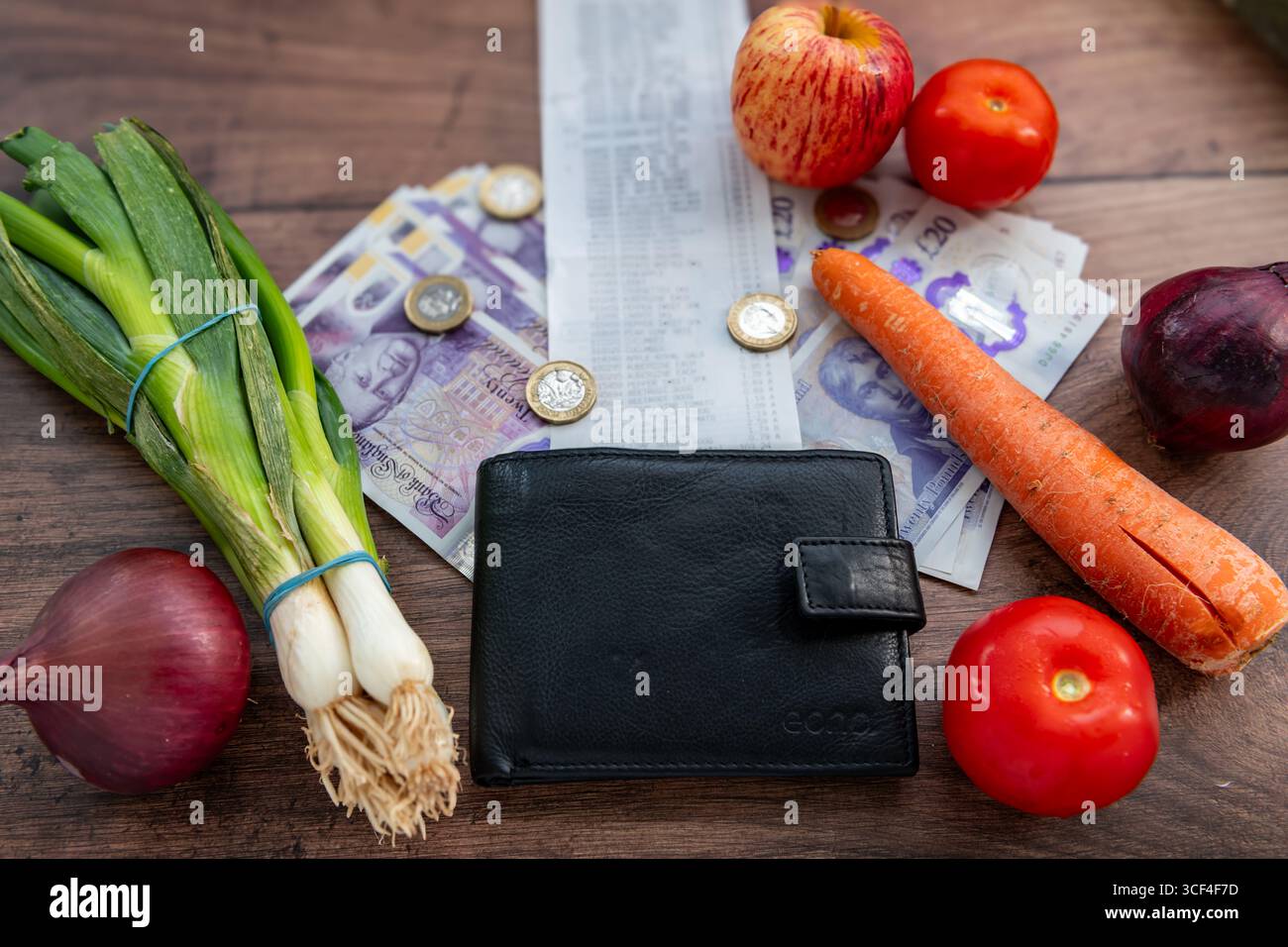 Un concetto del costo della vita nel Regno Unito con banconote Sterling, una ricevuta di spesa, una borsa e alcuni generi alimentari vegetali su un tavolo. Foto Stock