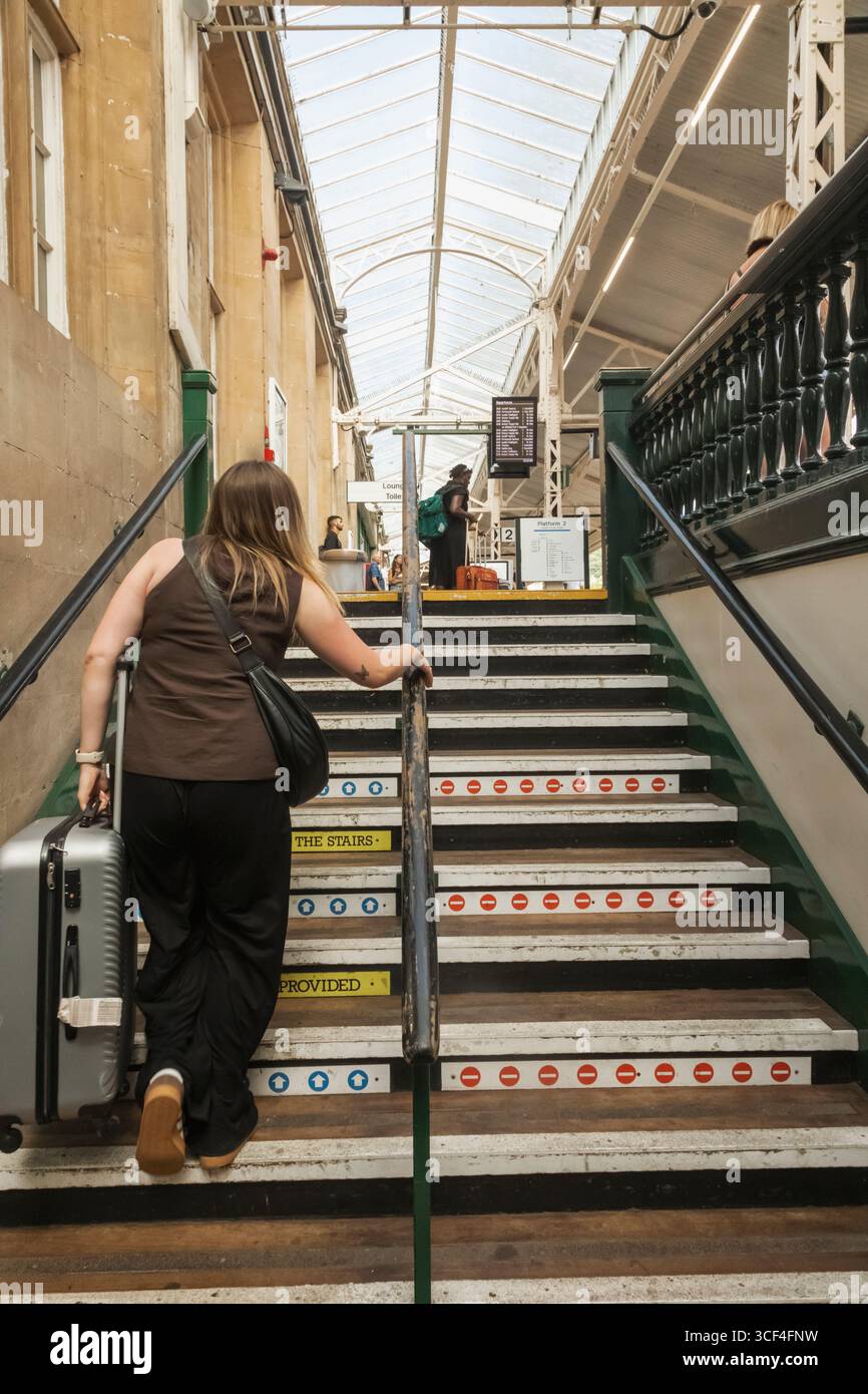 Inghilterra, Somerset, Bath, stazione ferroviaria di Bath Spa, passeggero femminile che trasporta valigia su scale della piattaforma Foto Stock