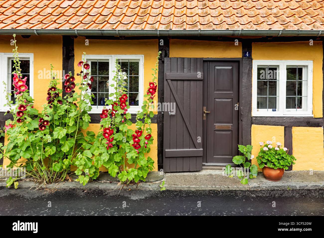 Intimo cottage giallo caratterizzato da porte in legno scuro e fiori colorati, a creare un'atmosfera calda, ideale per una tranquilla vita o una fuga di vacanza. Ronne t Foto Stock