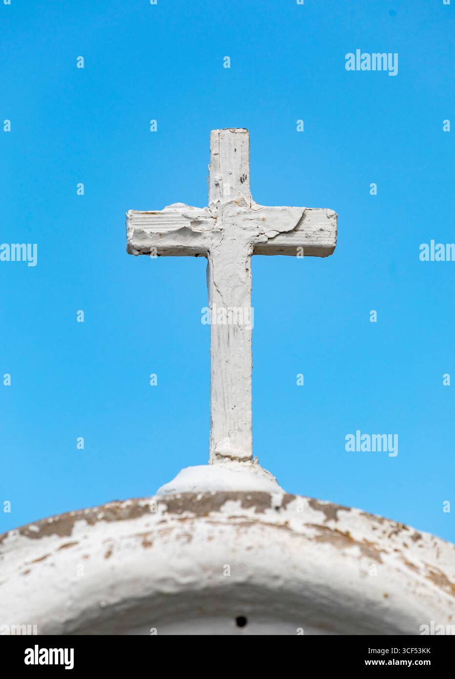 Semplice croce di legno bianco con vernice sbucciante in cima a una cupola bianca intemprata con cielo blu sullo sfondo, che evoca spiritualità, religione, fede e cristianesimo Foto Stock