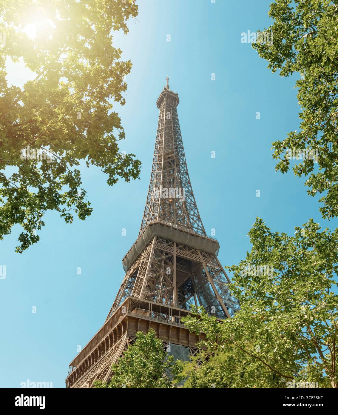 La Torre eiffel si innalza maestosamente nel cielo blu, incorniciata dal vibrante verde fogliame di alberi in una luminosa giornata estiva a parigi Foto Stock