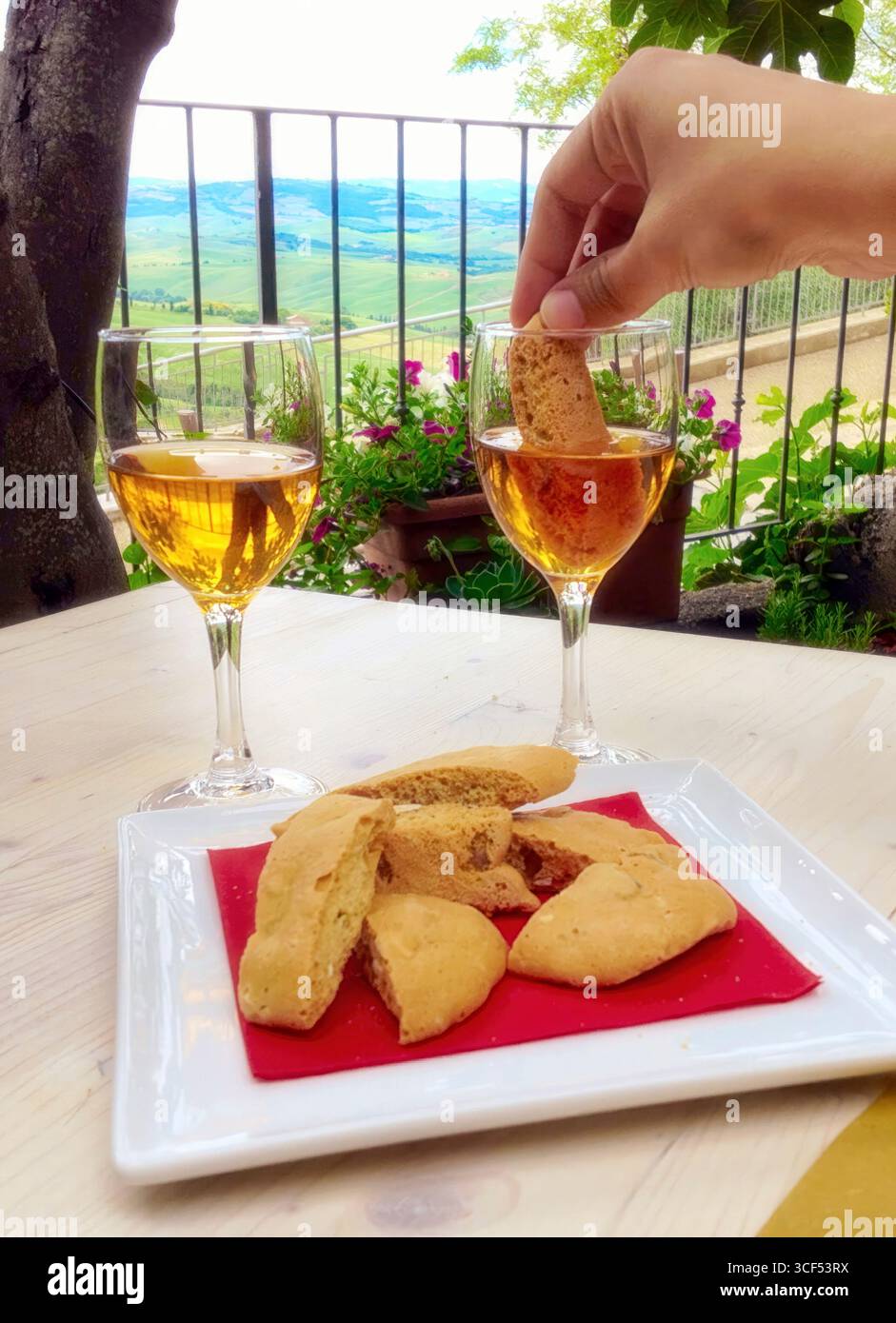 I tipici biscotti toscani chiamati cantucci o cantuccini sono immersi nel vino da dessert vin santo con vista sul paesaggio della val d'orcia a pienza, toscana, italia Foto Stock