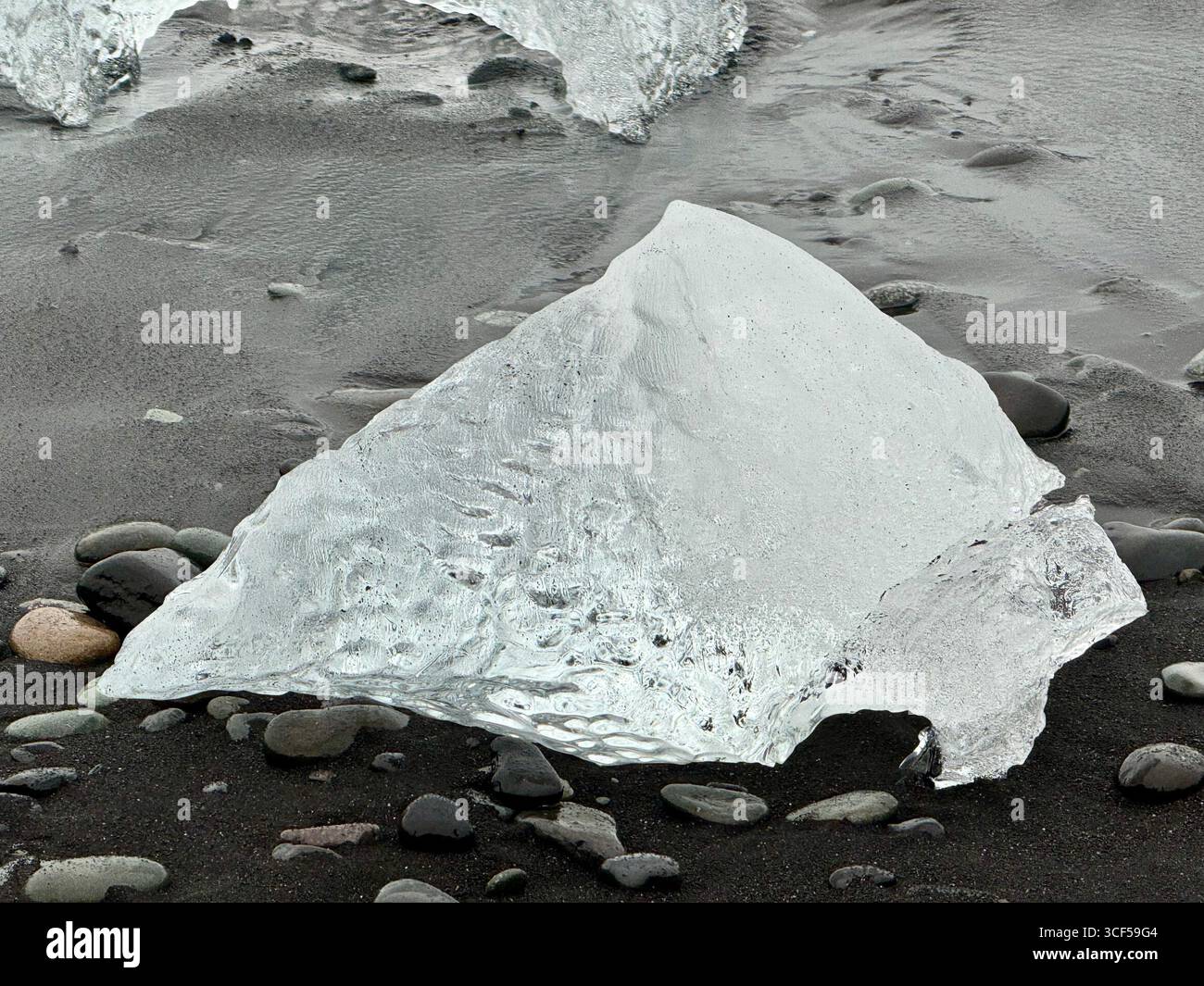 Un pezzo di ghiaccio a forma di piramide sulla sabbia nera presso l'iconica Diamond Beach in Islanda. Foto Stock