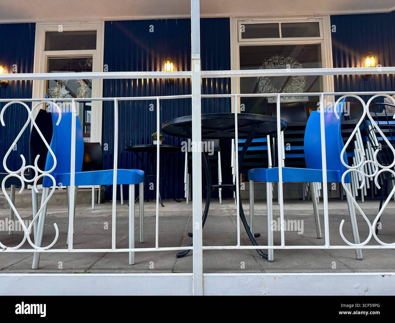 Sedie di colore blu luminoso e un tavolo nero contro un edificio blu con finiture bianche e ringhiera bianca sulla terrazza. - Immagine stock catturata con smartphone