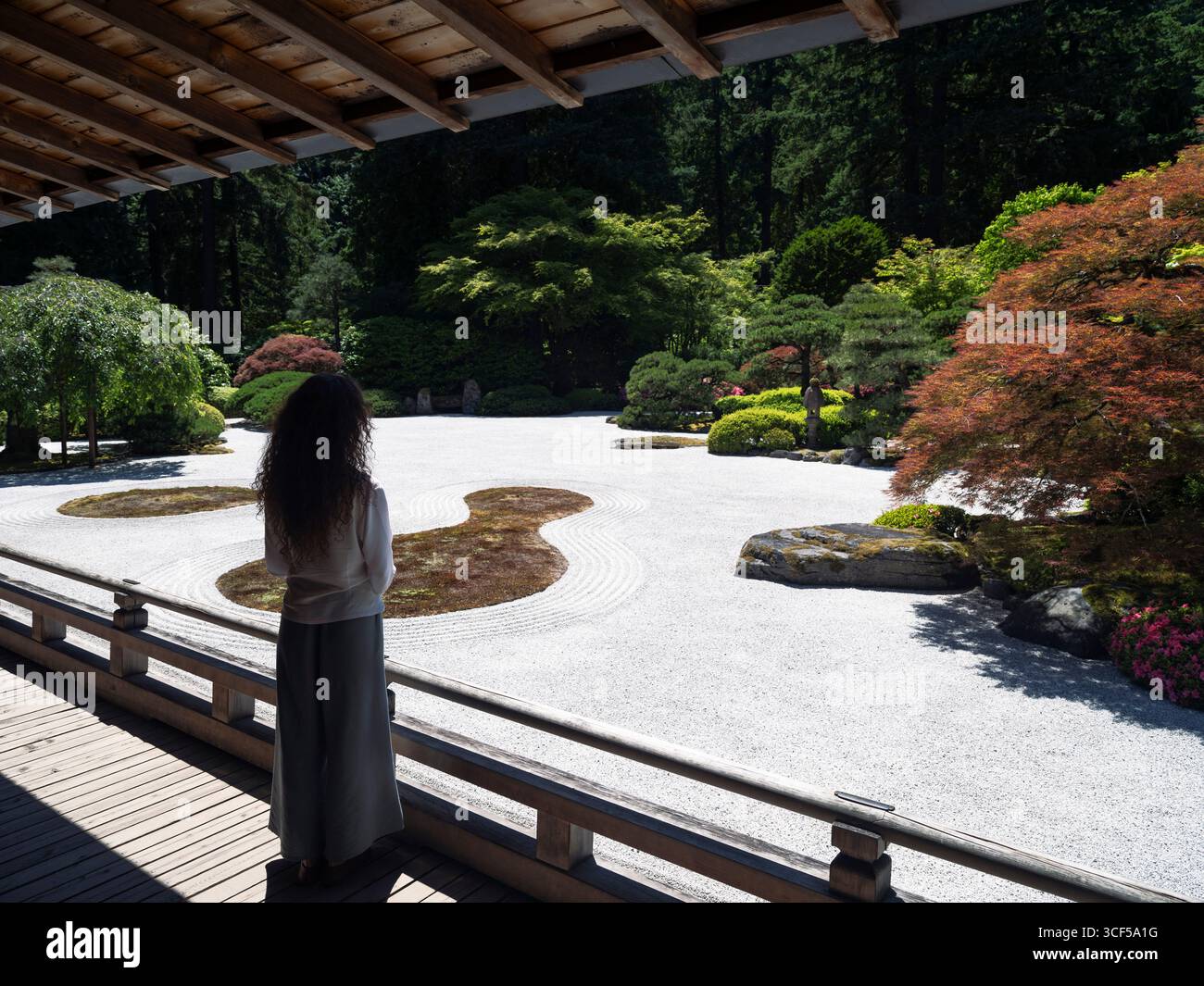 Donna che contempla un giardino di roccia zen giapponese in piedi su una terrazza di un padiglione nel Portland Japanese Garden, Oregon, Stati Uniti. Vista posteriore. Foto Stock