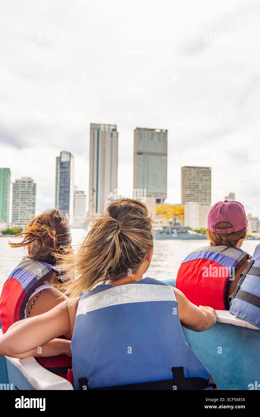 Tre persone con giubbotti salvagente si godono un giro in barca con vista sul moderno skyline di Cartagena, che mostra la bellezza della città storica. Foto Stock