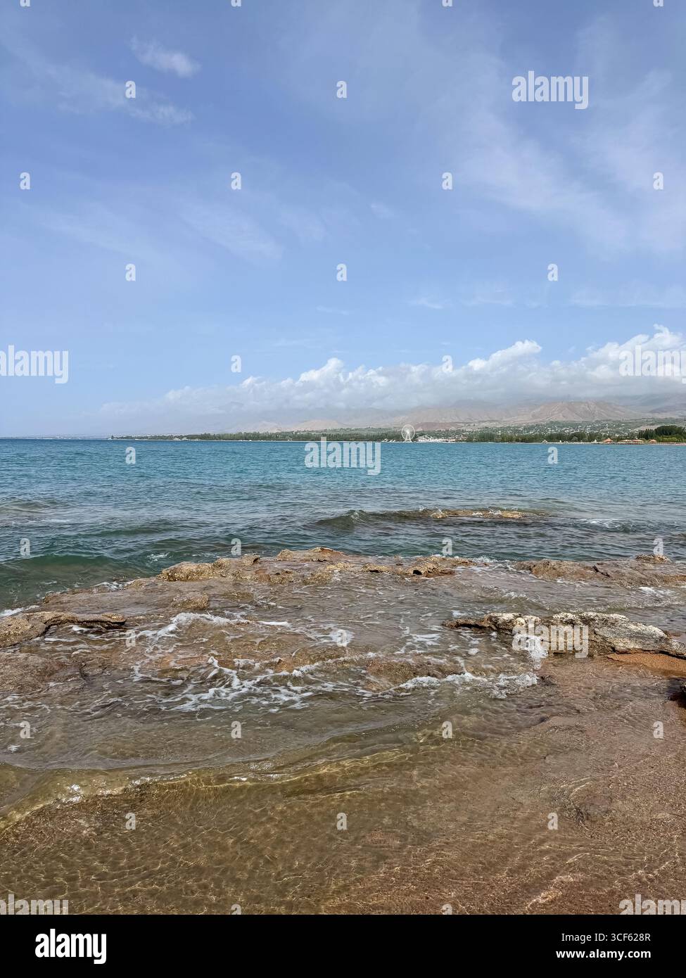 Costa rocciosa e acque limpide di Issyk-Kul sotto un vasto cielo. Foto Stock