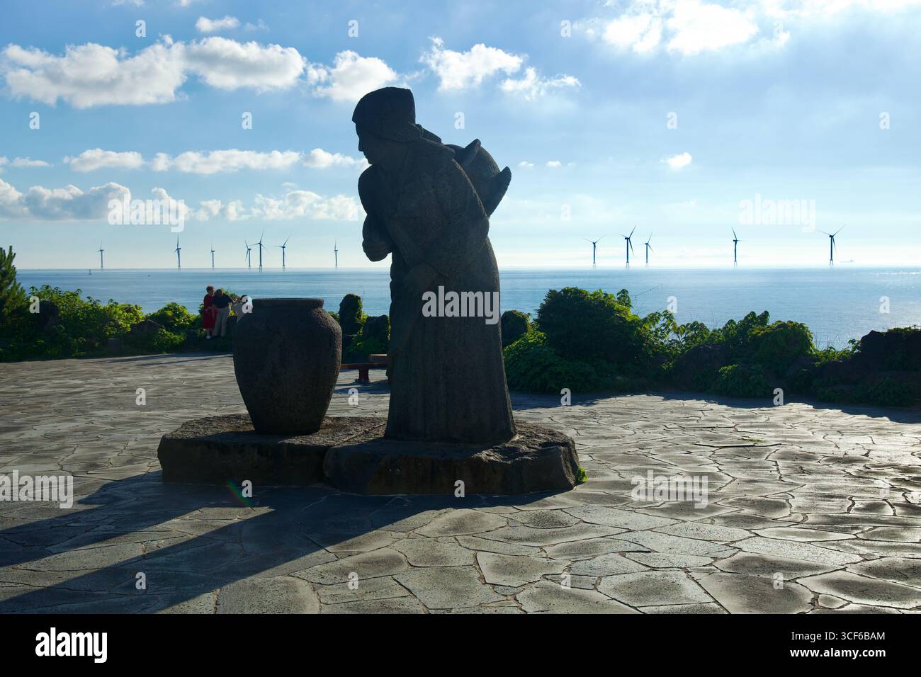 Una statua di granito di una donna con un vaso d'acqua si trova in un punto panoramico vicino al parco Aewol Handam Jeju Woman con una scultura di vaso d'acqua, che getta un lungo tratto Foto Stock