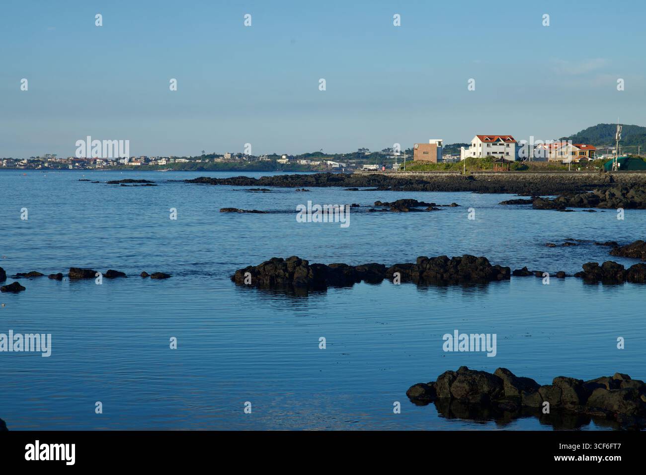 La costa rocciosa si estende a est da Gwideok verso Aewol, con affioramenti di lava sparsi in acque calme e quartieri di mare bassi che costeggiano il dist Foto Stock
