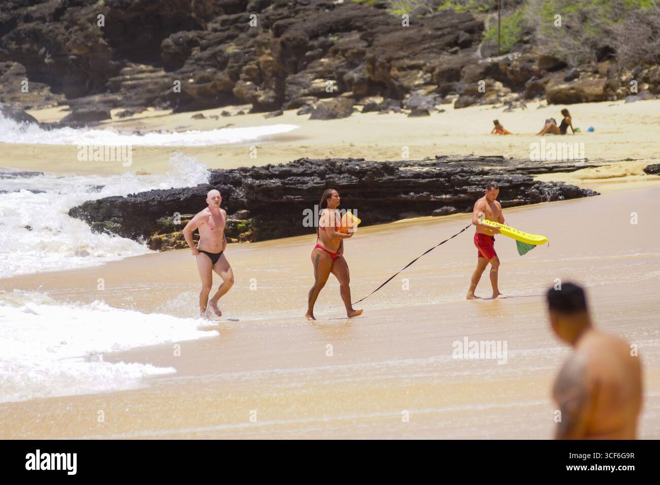 I bagnini si precipitano nel surf per salvare l'uomo in difficoltà al Sandy Beach Park di Honolulu, un momento urgente di coraggio e precisione sul bordo dell'oceano. Foto Stock
