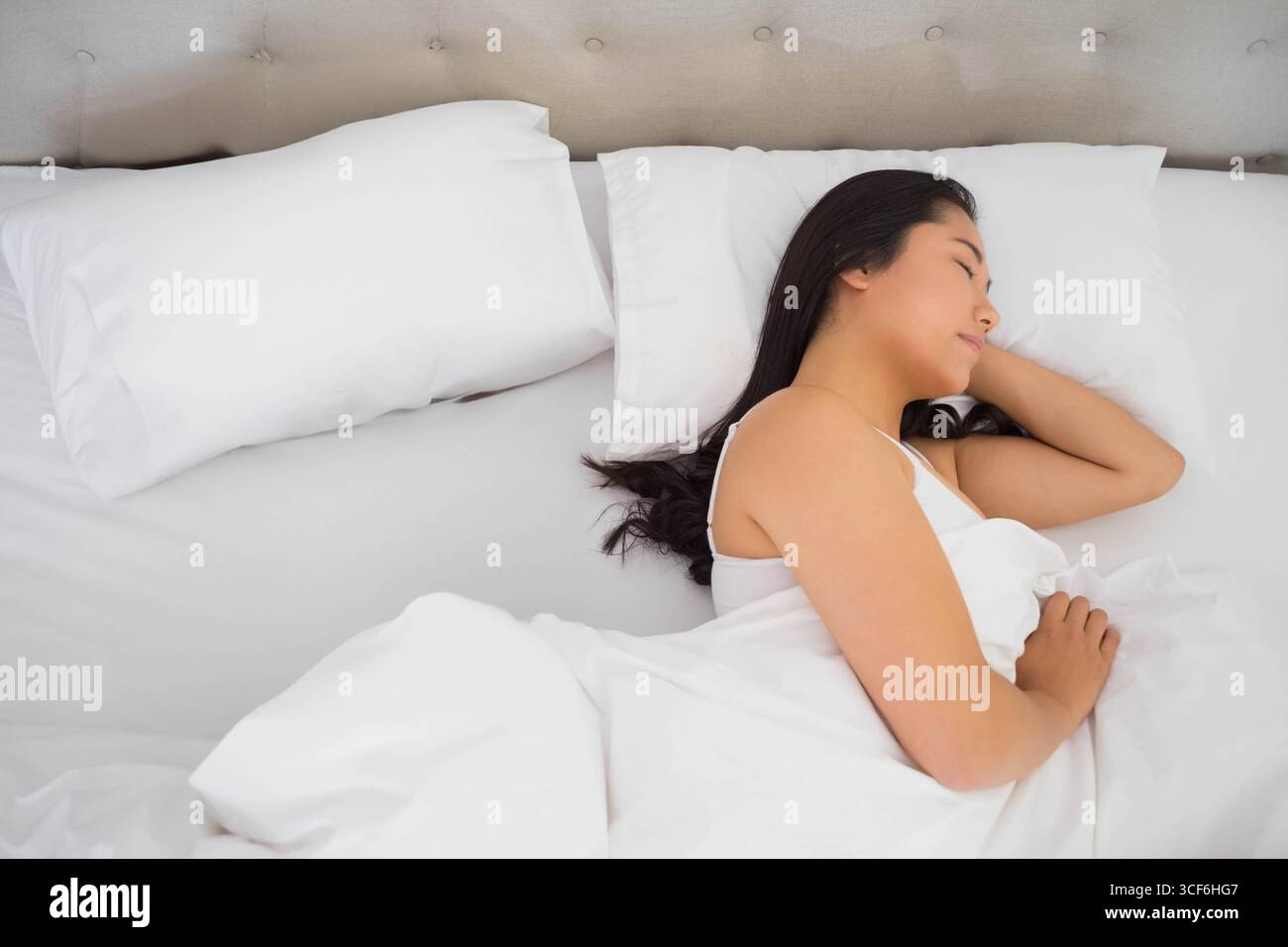 Donna coreana sdraiata su un lato del letto in camera da letto con piumone bianco, testiera e spazio fotocopie Foto Stock