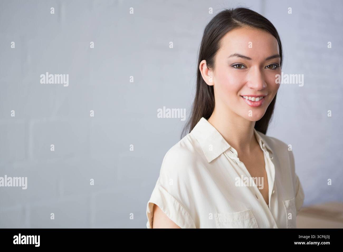 Donna asiatica che sorride, indossa una camicetta e si trova in piedi davanti a un muro in mattoni dipinti in studio, copia spazio Foto Stock
