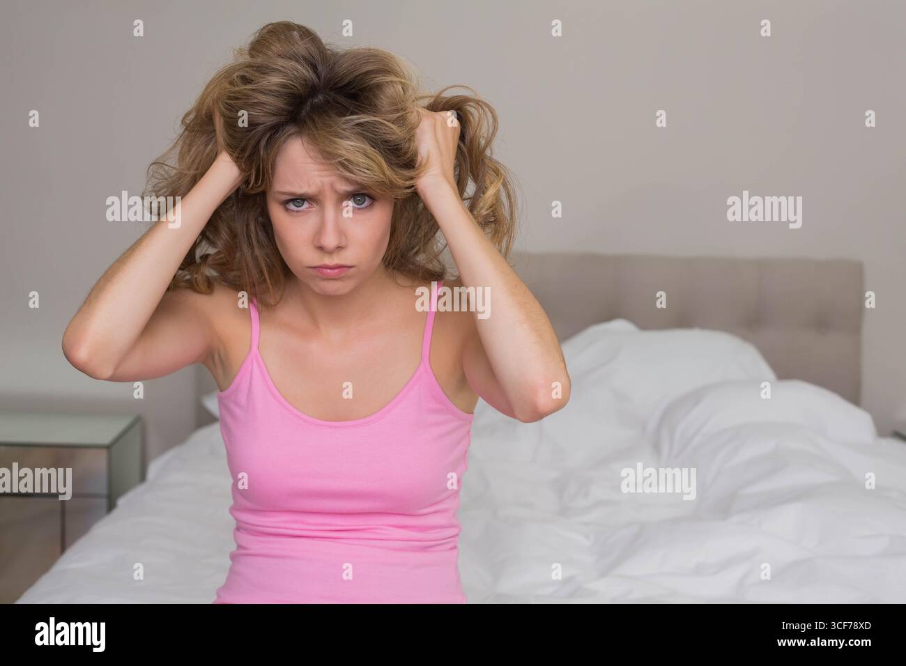 Capelli femminili tiranti sul letto in camera da letto con comodino a specchio, testiera beige bianca Foto Stock