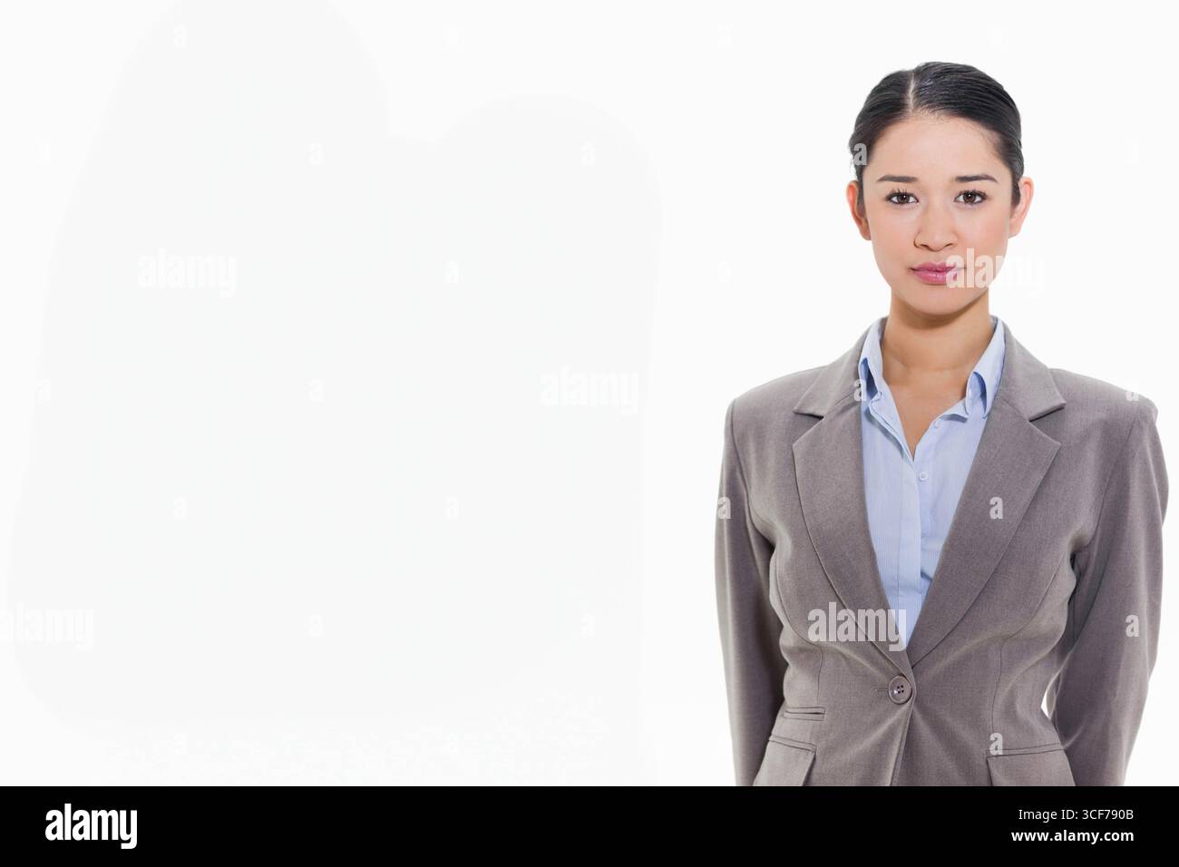 Donna asiatica in piedi su sfondo bianco con vestito grigio e camicia blu con colletto, copia spazio Foto Stock