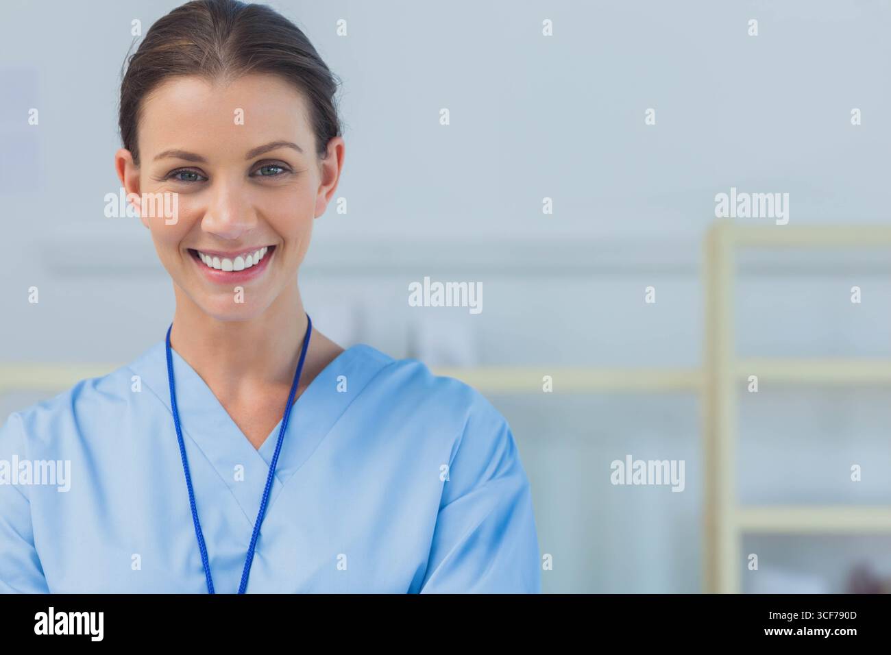 Infermiere che indossa scrub azzurro con cordone in piedi e sorride nella scaffalatura della sala esame, spazio di copia Foto Stock
