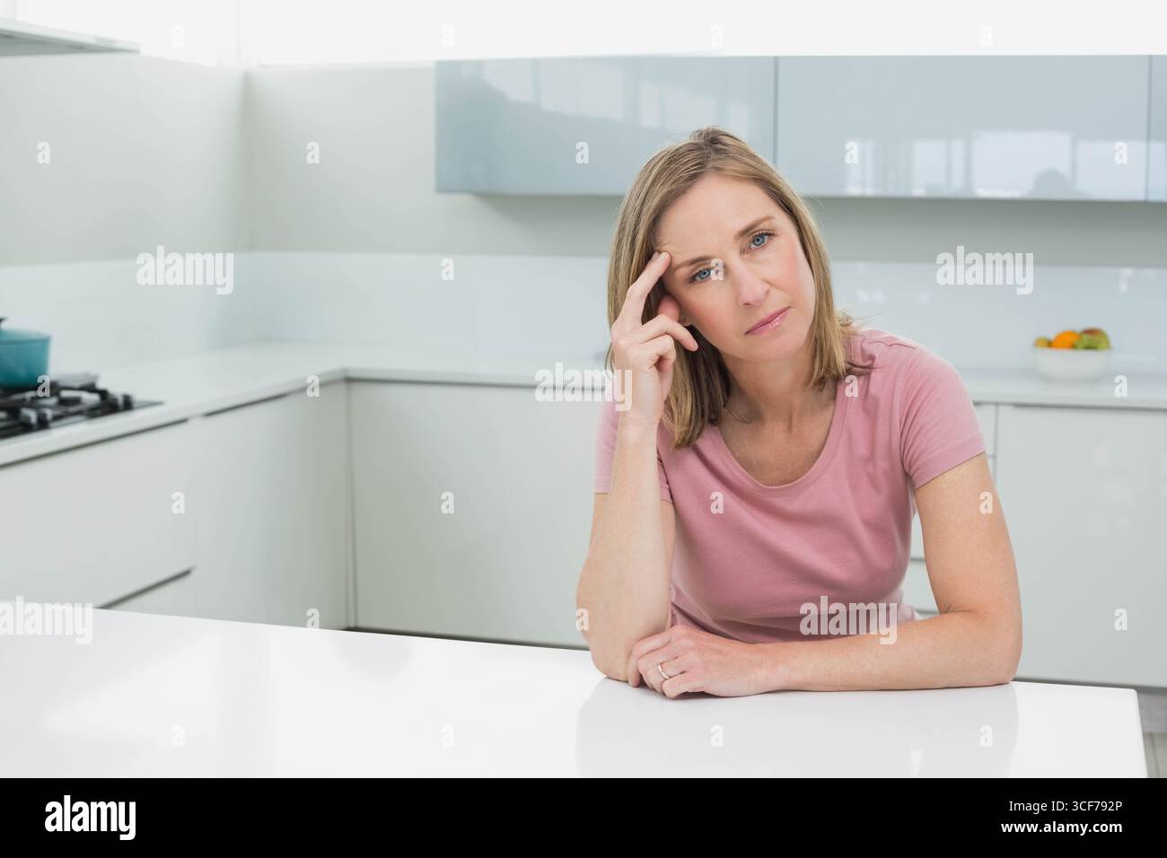 Donna di mezza età che riposa il gomito sull'isola della cucina accanto alla stufa a gas e guarda in avanti, copia lo spazio Foto Stock