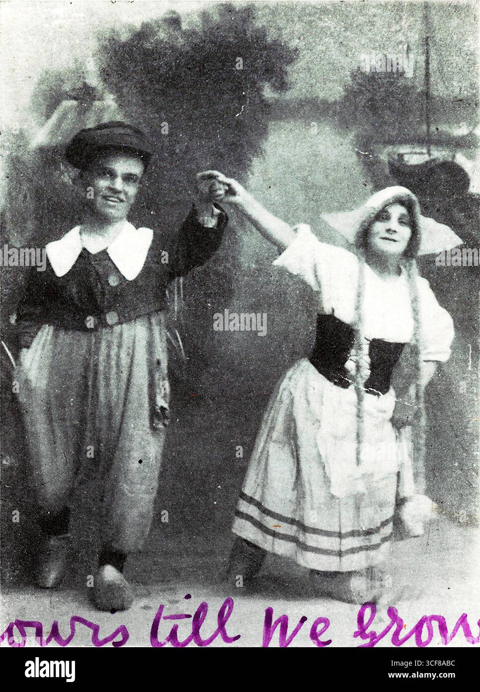 Pubblicata da J. Waddington di Leeds e Londra e datata 5 marzo 1920, questa cartolina presenta Pip e Melinda, creatori di mirti in miniatura, posati mano nella mano davanti a uno sfondo pastorale dipinto di alberi e una barca sull'acqua. I loro costumi teatrali evocano giocosa fantasia edoardiana: PIP indossa un vestito sciolto con un grande colletto bianco e un cappello, mentre Melinda indossa un abito a corsetto e un cofano. La didascalia "Yours till We Grow" aggiunge umorismo romantico e fascino consapevole, combinando prestazioni, affetto e narrazione visiva in forma miniaturizzata. Foto Stock