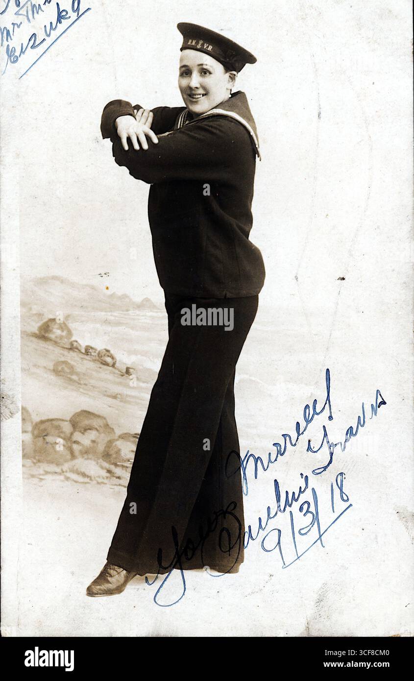 Pauline Travis, una sosia maschile attiva nel 1918, è raffigurata in questo ritratto in bianco e nero di studio con indosso un'uniforme da marinaio e un cappello incisi "R.N." e "V.R.", che evocano le affiliazioni della Royal Navy e della riserva volontaria. La sua posizione sicura, le braccia incrociate e sorridenti, riflette il bravado teatrale tipico degli atti di varietà edoardiani. Uno sfondo marino dipinto e la sua iscrizione scritta a mano (“Yours Sincerely, Pauline Travis, 9/3/18”) aggiungono intimità e fascino. Come interprete all'Argyle Theatre of Variety di Birkenhead, Travis incarna la resilienza in tempo di guerra e il gioco di genere sul palcoscenico popolare. Foto Stock