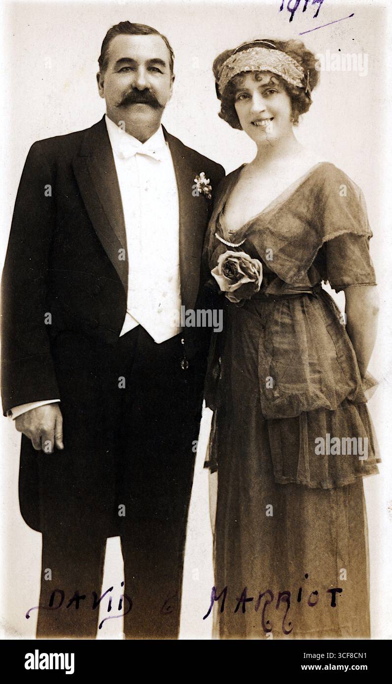 David & Marriot, un duo teatrale attivo durante la prima guerra mondiale, sono raffigurati in un ritratto in stile seppia pubblicato da Charles e Russell di Belfast nel 1917. Il loro abbigliamento formale, il suo smoking e i baffi prominenti, il suo abito e la fascia abbelliti, suggerisce una raffinata presenza scenica, probabilmente in spettacoli musicali o drammatici. I nomi e la data scritti a mano evocano un momento di significato personale o professionale, mentre la finitura tattile e la provenienza regionale della cartolina riflettono la miscela di intrattenimento, ephemera e risonanza emotiva dell'epoca. Foto Stock