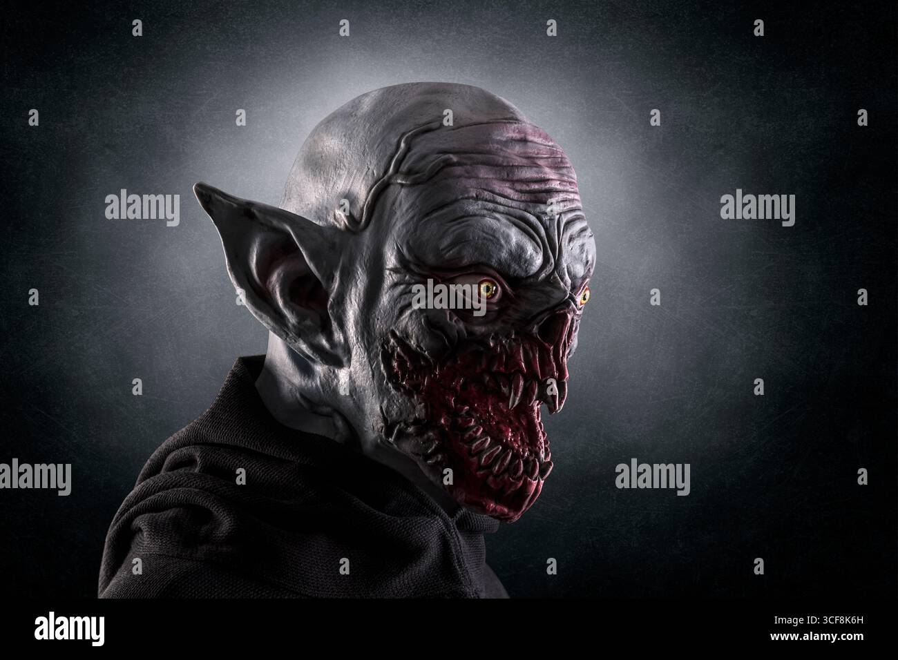 Ritratto di un mostro con zanne nitide su sfondo nebbioso scuro. In questa foto è stata usata una maschera in silicone. Foto Stock