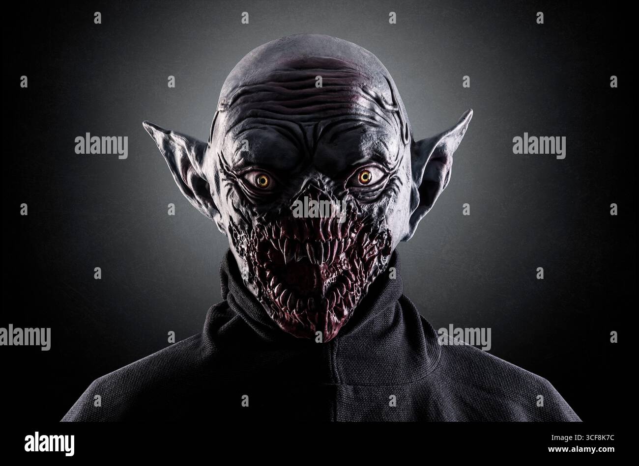 Ritratto di un mostro con zanne nitide su sfondo nebbioso scuro. In questa foto è stata usata una maschera in silicone. Foto Stock