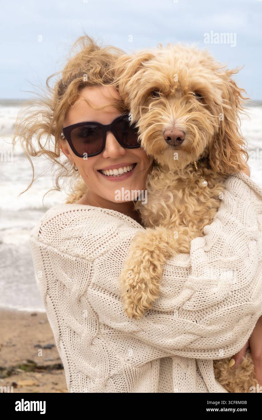 Un ritratto ravvicinato di una donna felice e sorridente e del suo carino cane Cockapoo sulla spiaggia di Saltburn-by-the-Sea nel North Yorkshire, Regno Unito. Foto Stock