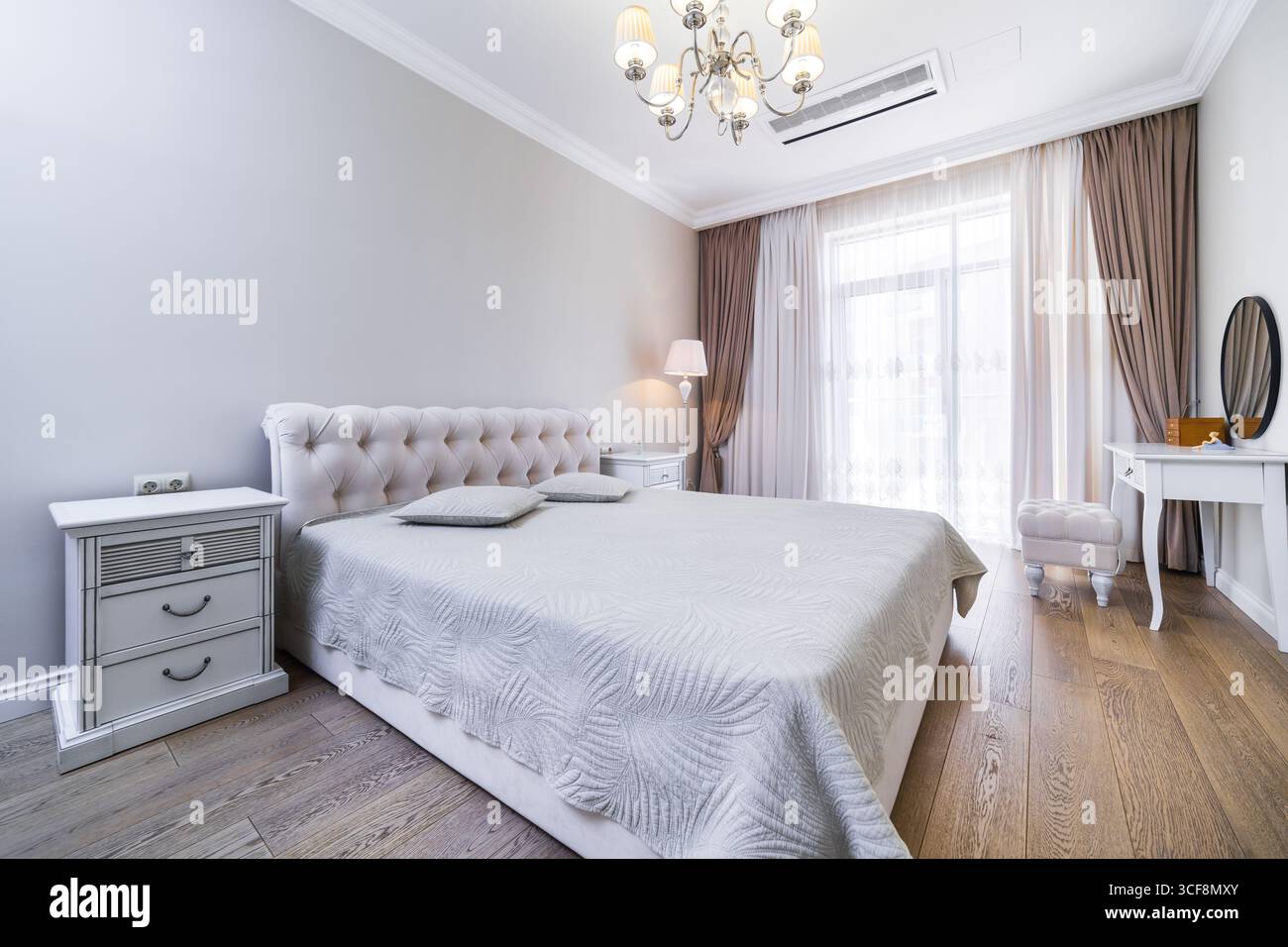Una camera con una nuova e intima ristrutturazione in tonalità grigio-beige. Ampio letto matrimoniale con coperta grigia. Comodini e un tavolo in stile classico. Foto Stock