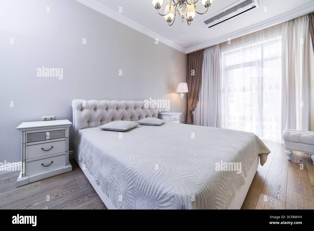 Una camera con una nuova e intima ristrutturazione in tonalità grigio-beige. Ampio letto matrimoniale con coperta grigia. Comodini e un tavolo in stile classico. Foto Stock