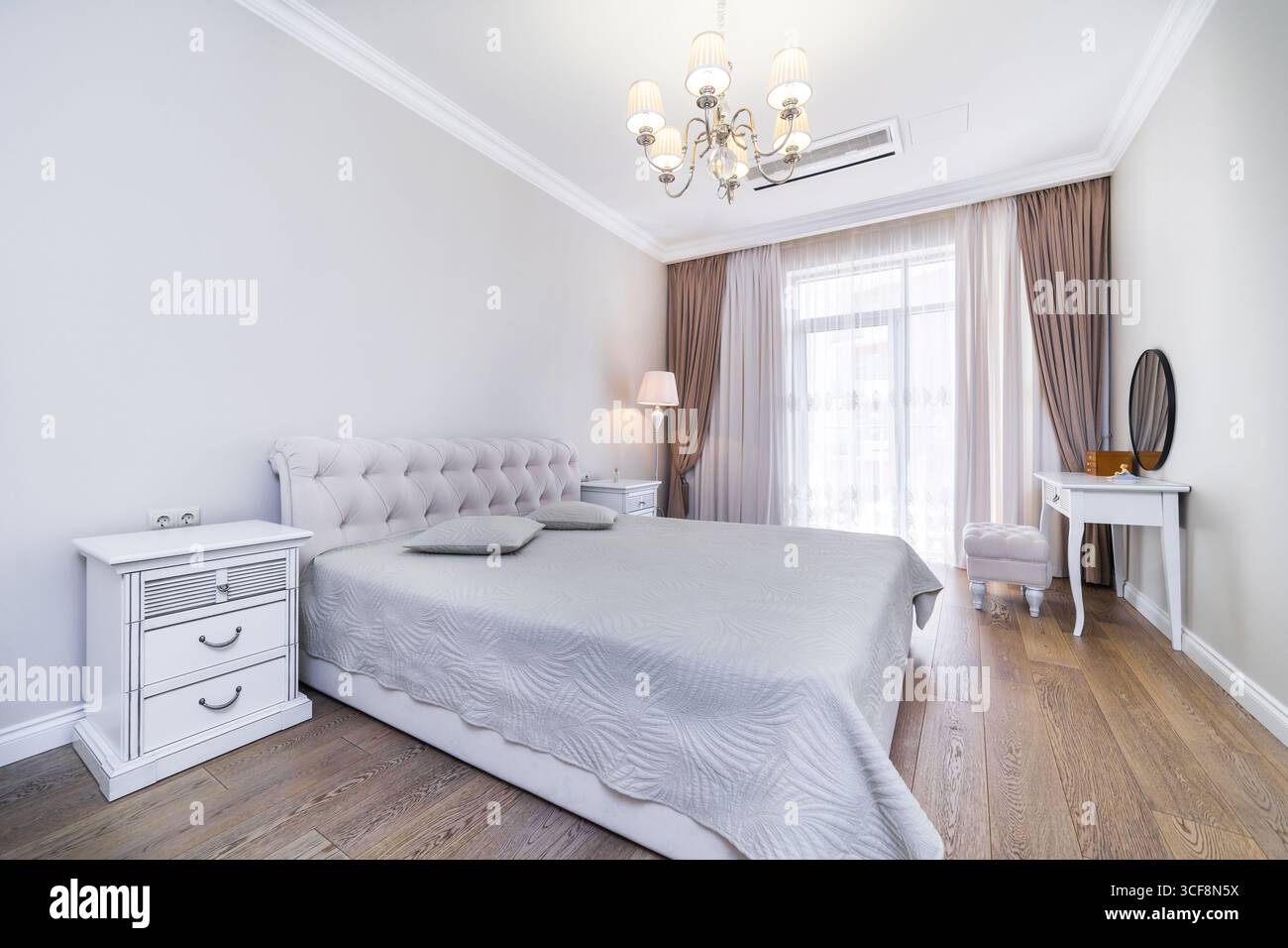 Una camera con una nuova e intima ristrutturazione in tonalità grigio-beige. Ampio letto matrimoniale con coperta grigia. Comodini e un tavolo in stile classico. Foto Stock