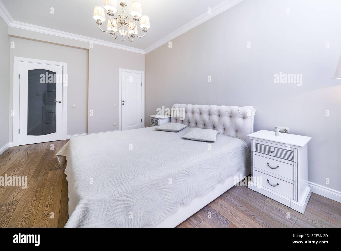Una camera con una nuova e intima ristrutturazione in tonalità grigio-beige. Ampio letto matrimoniale con coperta grigia. Comodini e un tavolo in stile classico. Foto Stock