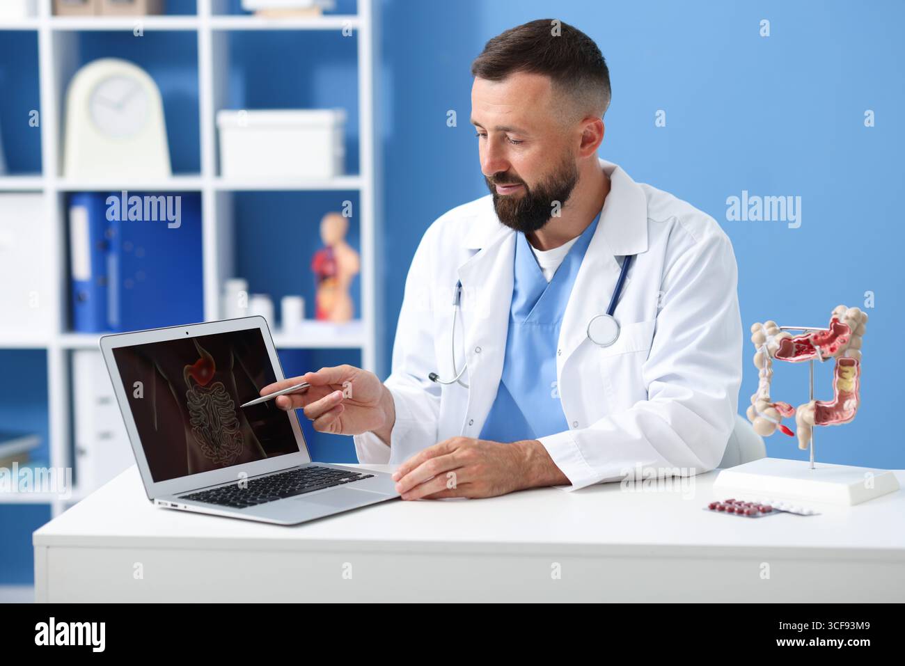 Gastroenterologo che mostra lo schermo con illustrazione del tratto digerente al tavolo in clinica Foto Stock