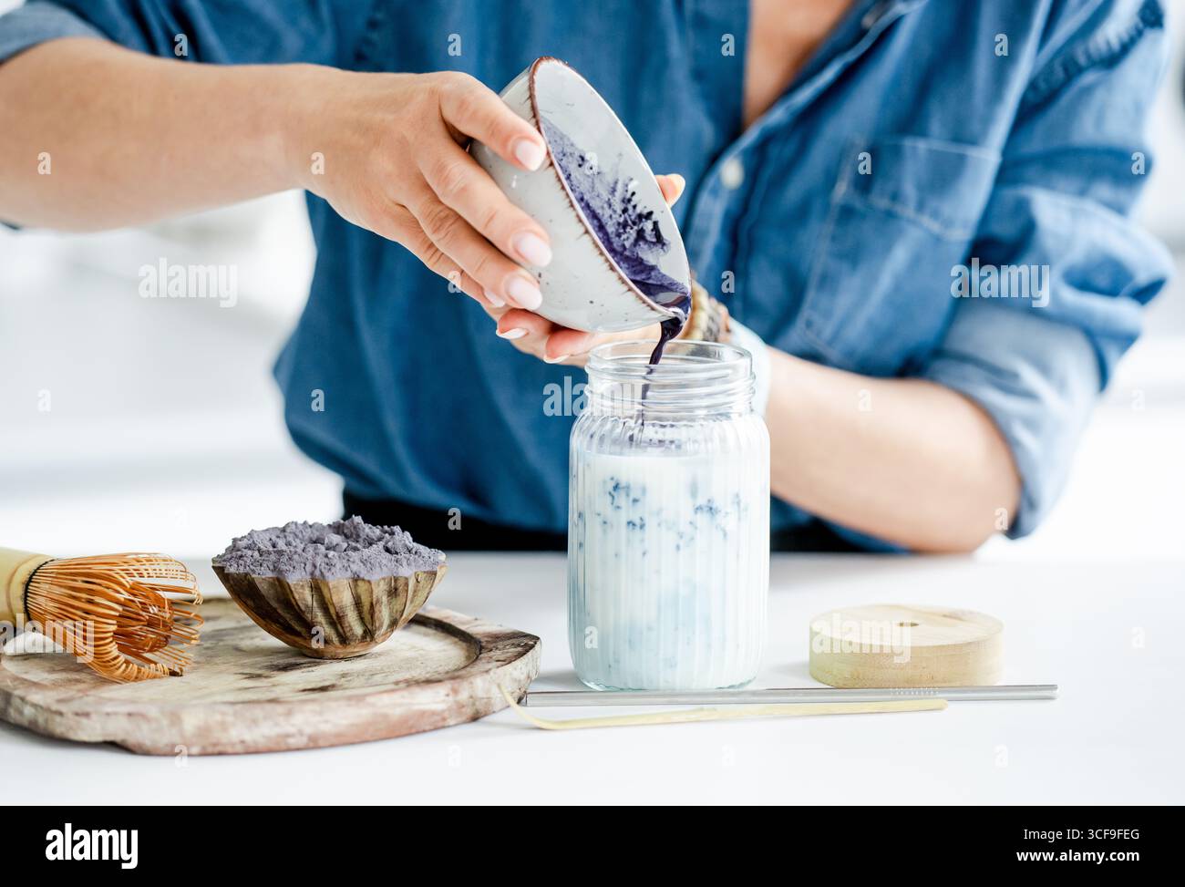 La donna versa Un Matcha latte con ghiaccio e latte in Un barattolo Foto Stock