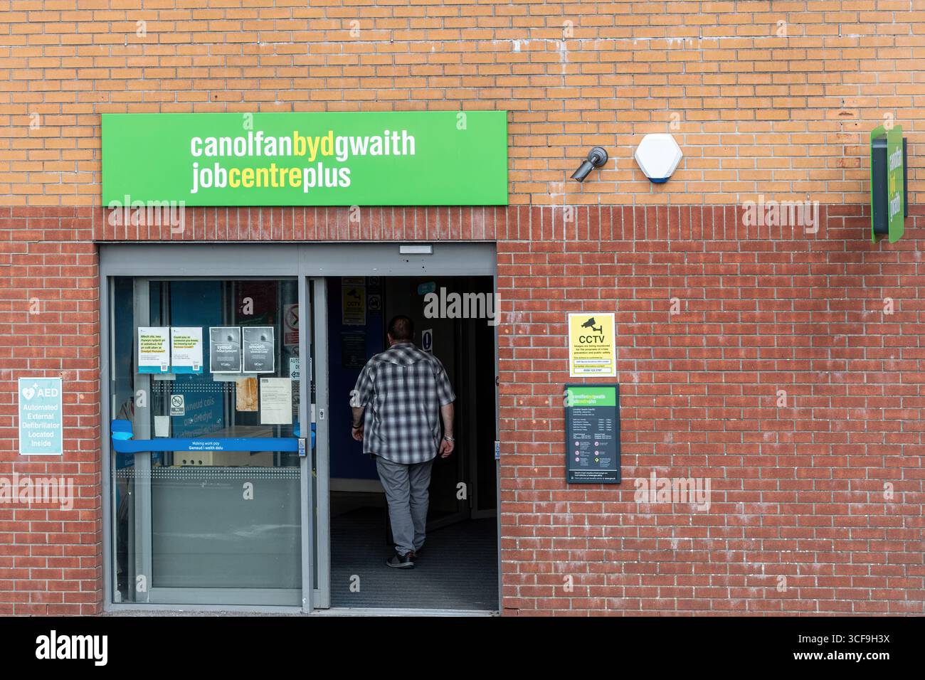 Uomo che entra in un centro di lavoro a Caerphilly, Galles, Regno Unito. Insegna bilingue Canolfan BYD Gwaith in gallese, Job Centre Plus in inglese Foto Stock