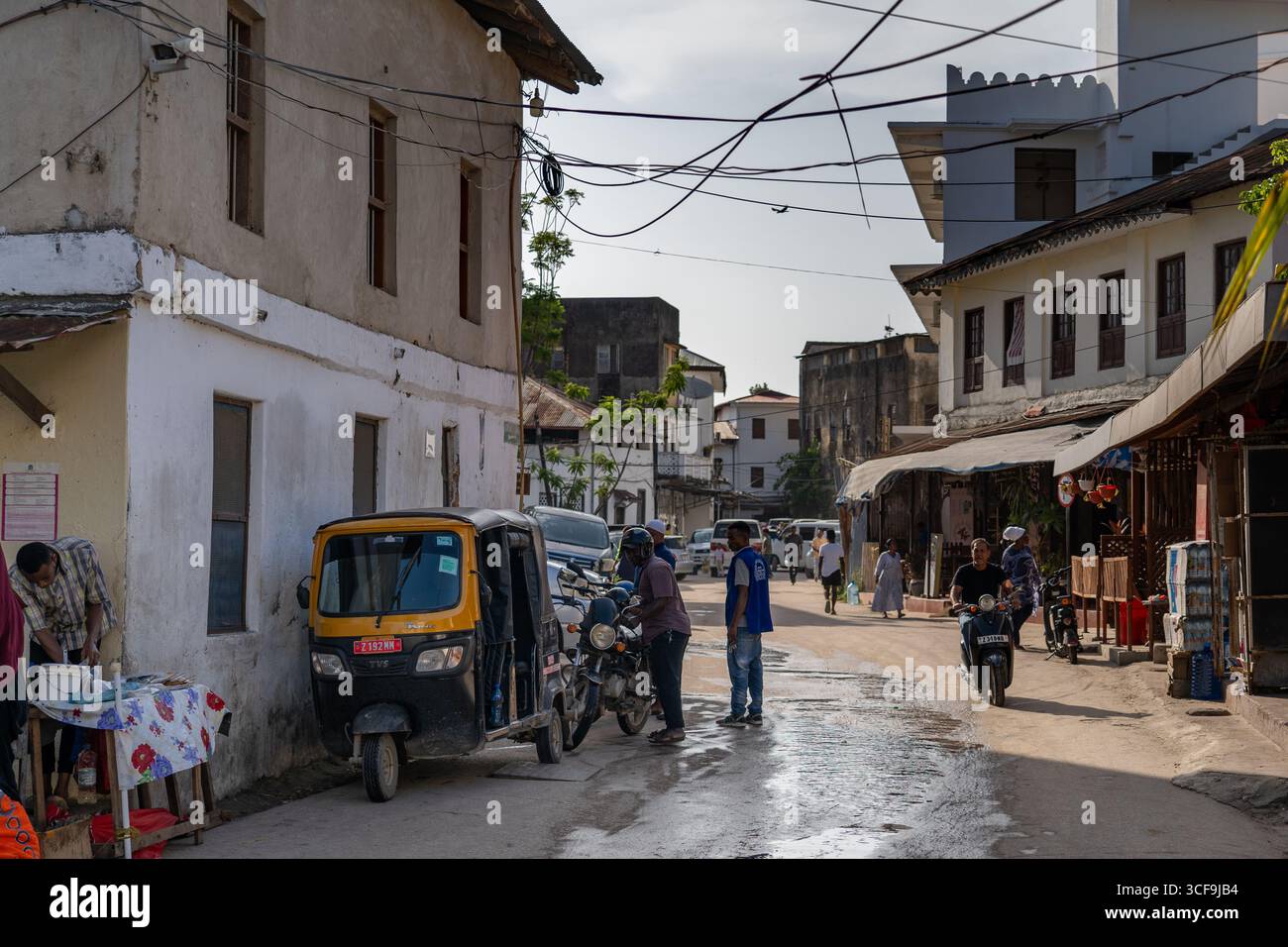 Strada con tuk tuk e venditori locali a Stone Town, Zanzibar Foto Stock