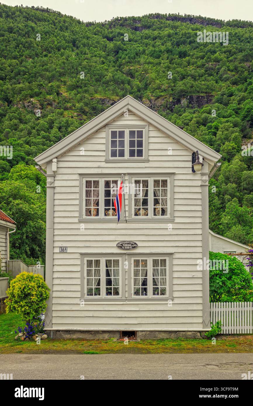Casa tradizionale di Lærdalsøyri. Una classica casa in legno bianco con una piccola bandiera norvegese, adagiata sullo sfondo di una montagna boscosa verde. Foto Stock