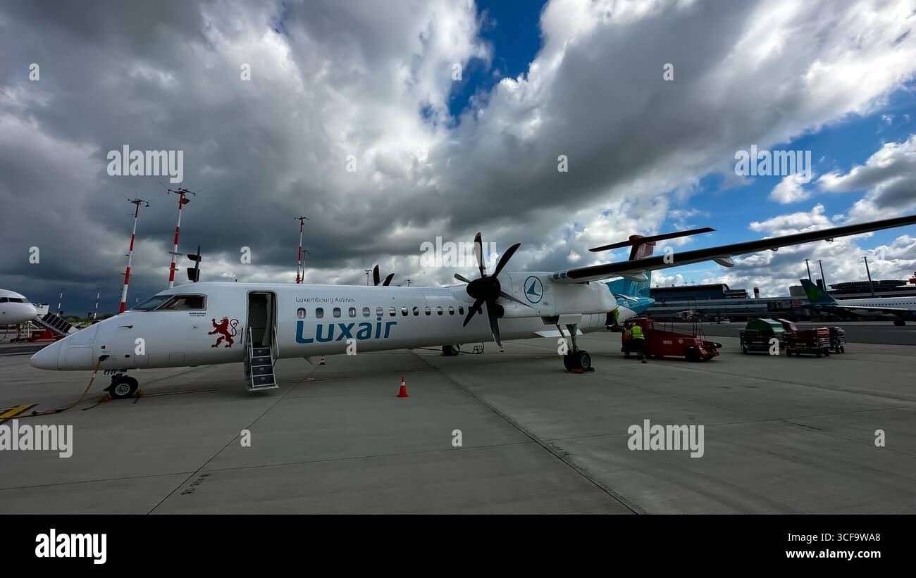 Un turboelica Luxair Dash 8 Q400 è parcheggiato sull'asfalto sotto un cielo spettacolare e nuvoloso in un aeroporto. Foto Stock