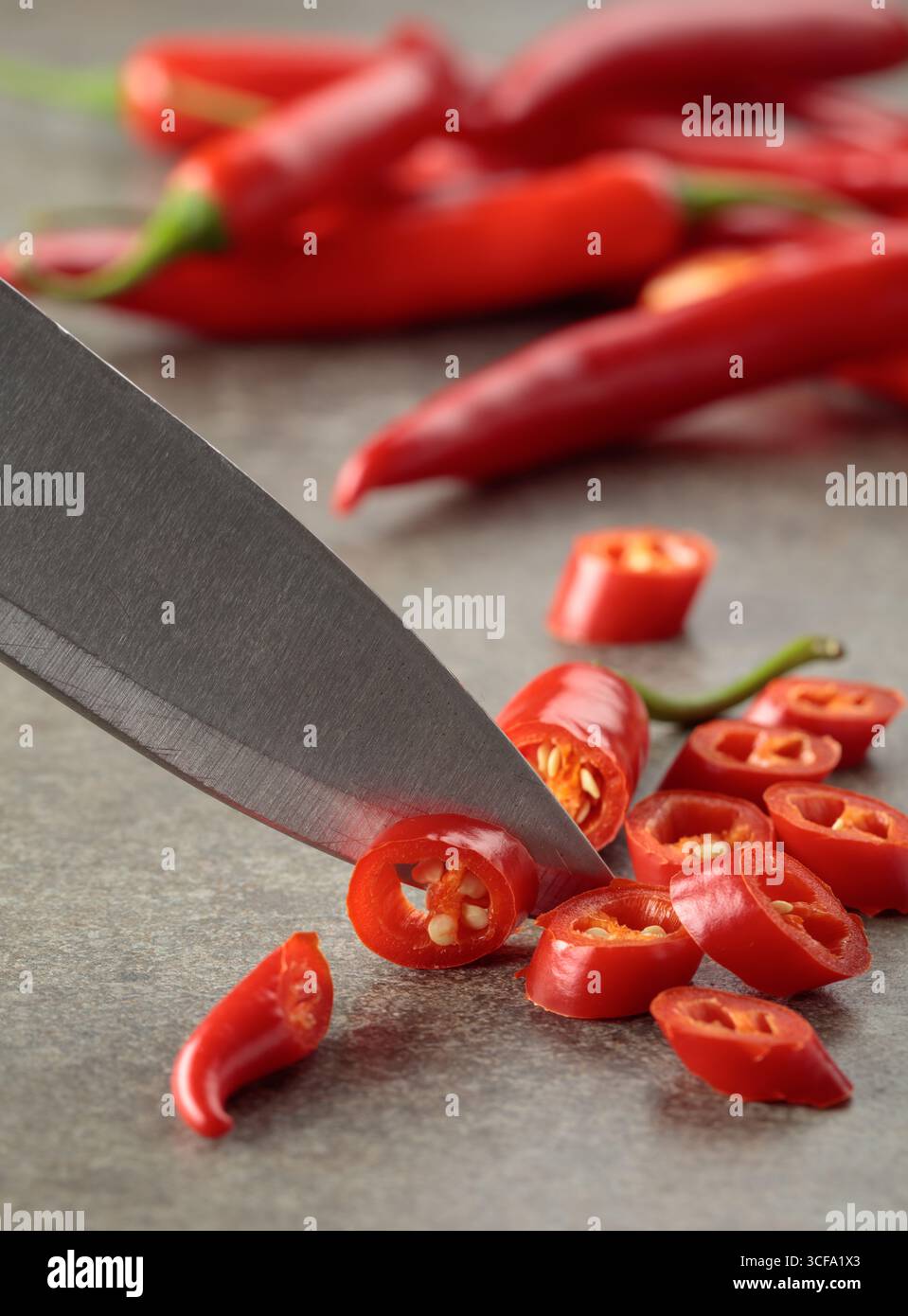 Coltello da cucina e peperoncini rossi freschi a fette. Foto Stock