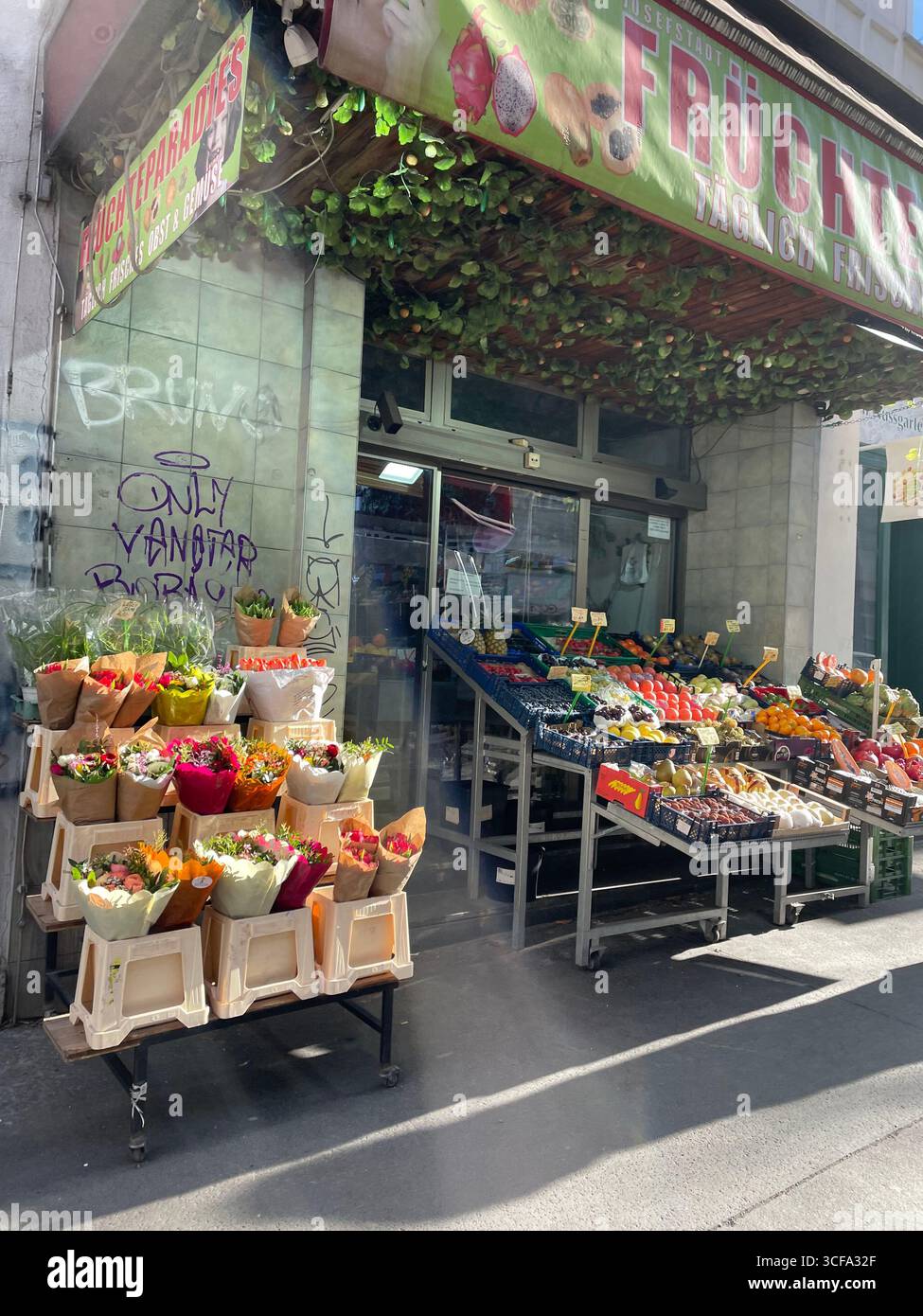 Vienna, Austria - 10 gennaio 2025: Scaffali illuminati dal sole in un negozio di alimentari locale in una strada della capitale; frutta e verdura fresche in una soleggiata giornata invernale - Immagine stock catturata con smartphone