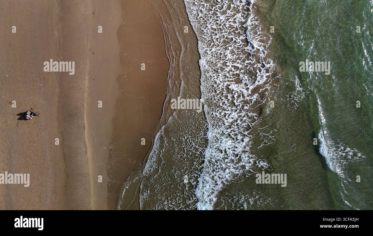 Le sabbie dorate si estendono accanto alle onde calmanti, dove una figura solitaria gode dell'atmosfera serena di un tramonto. I colori della natura si fondono magnificamente Foto Stock