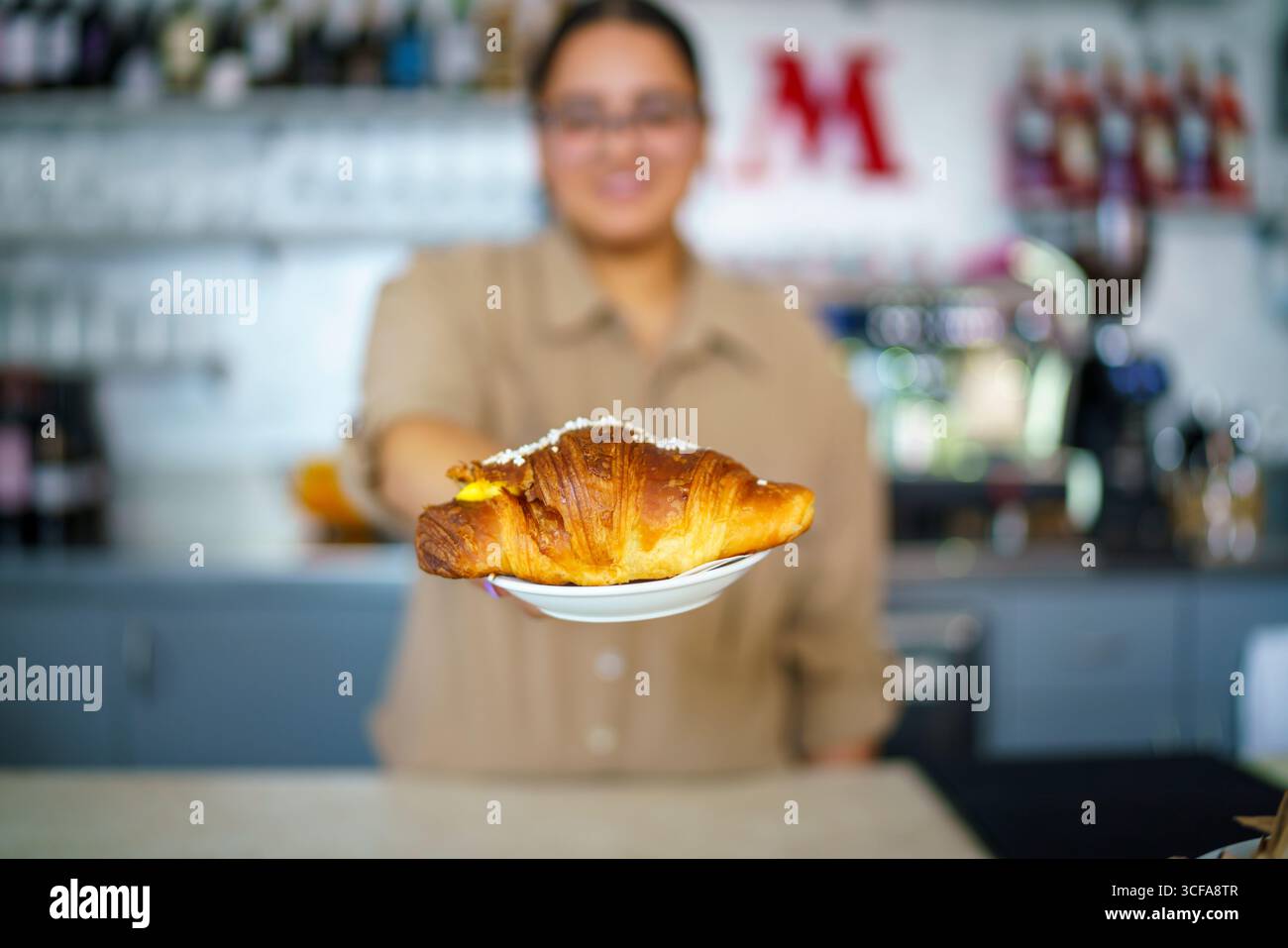 Cremona, Italia 25 luglio 2025 Barista serve un delizioso croissant appena sfornato ripieno di crema pasticcera e condito con zucchero granulato, offeri Foto Stock
