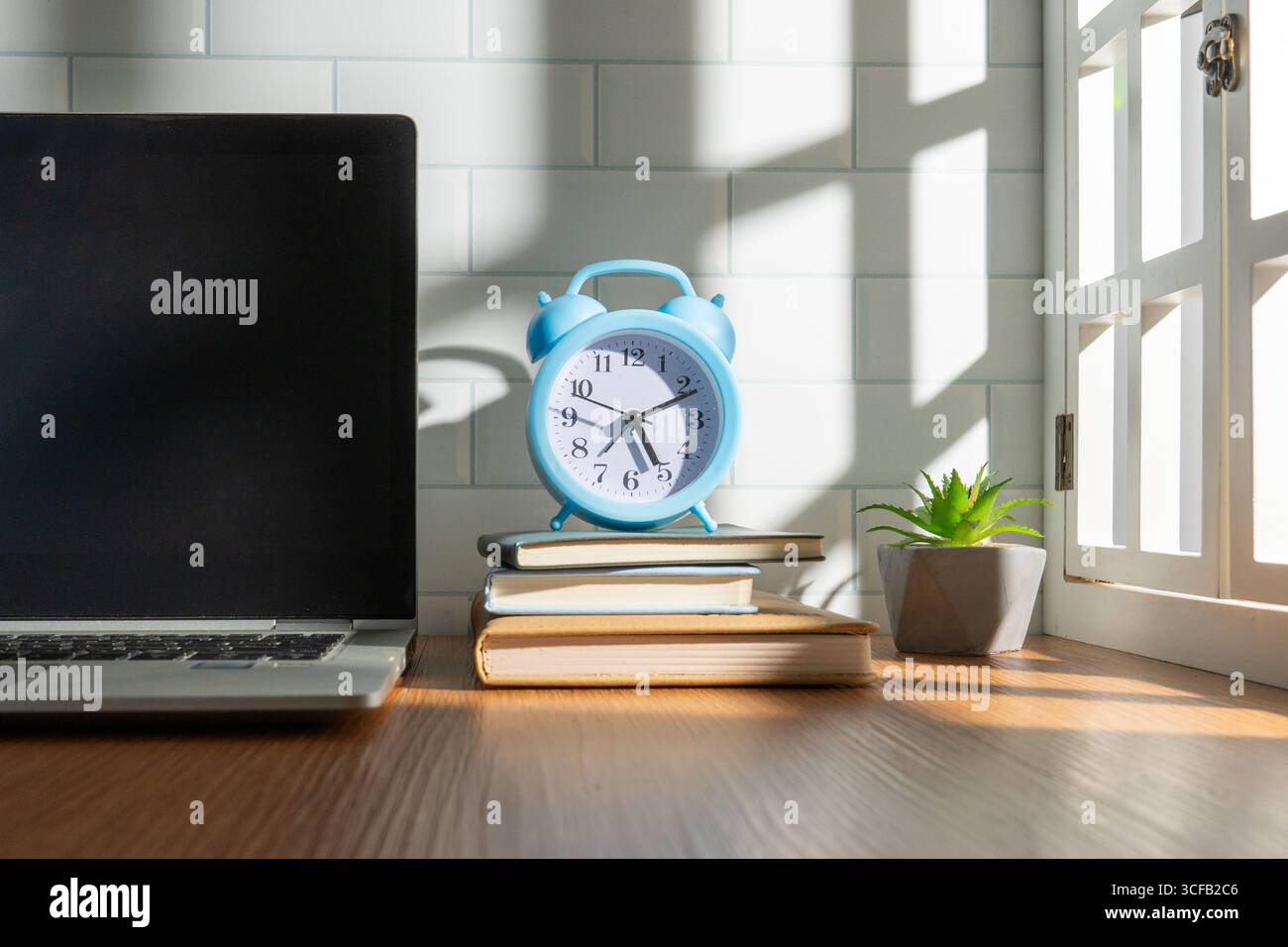 Una scrivania in legno con un computer portatile, libri, una sveglia e una pianta succulenta. Concetto di produttività, apprendimento e gestione del tempo. Foto Stock