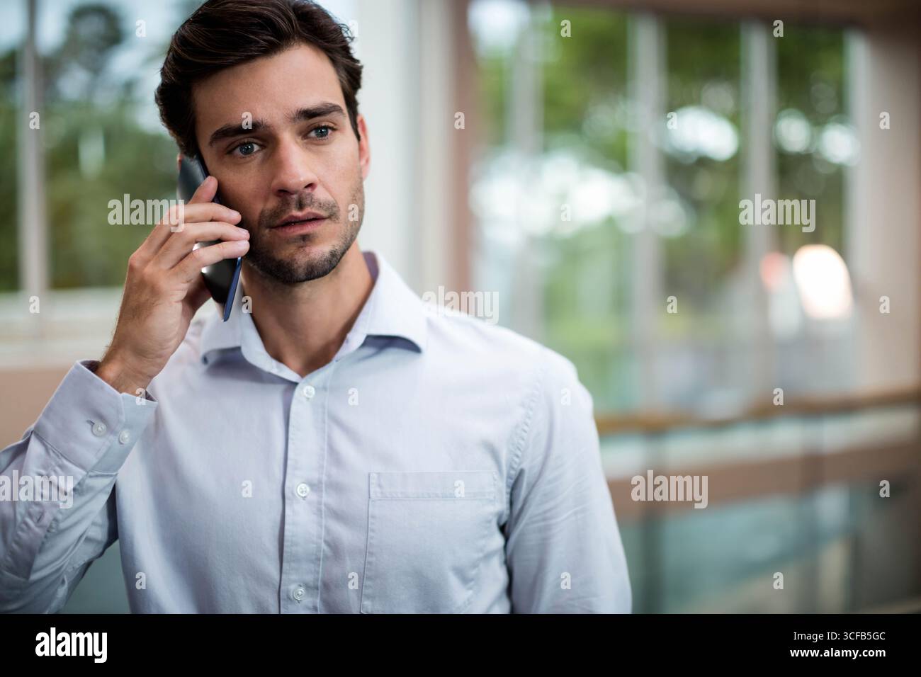 Uomo medio adulto che indossa una camicia blu in piedi nella hall dell'edificio tenendo in mano lo smartphone Foto Stock