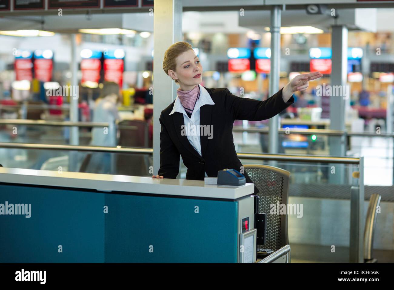 Una donna bianca che fa il check-in guida i passeggeri che puntano direttamente al bancone dell'aeroporto affollato con scanner Foto Stock