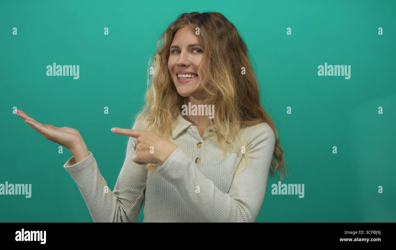 Una donna che punta a mano lo sfondo di uno schermo di colore verde palma, giovane e sorridente, offre un potenziale promozionale. Foto Stock