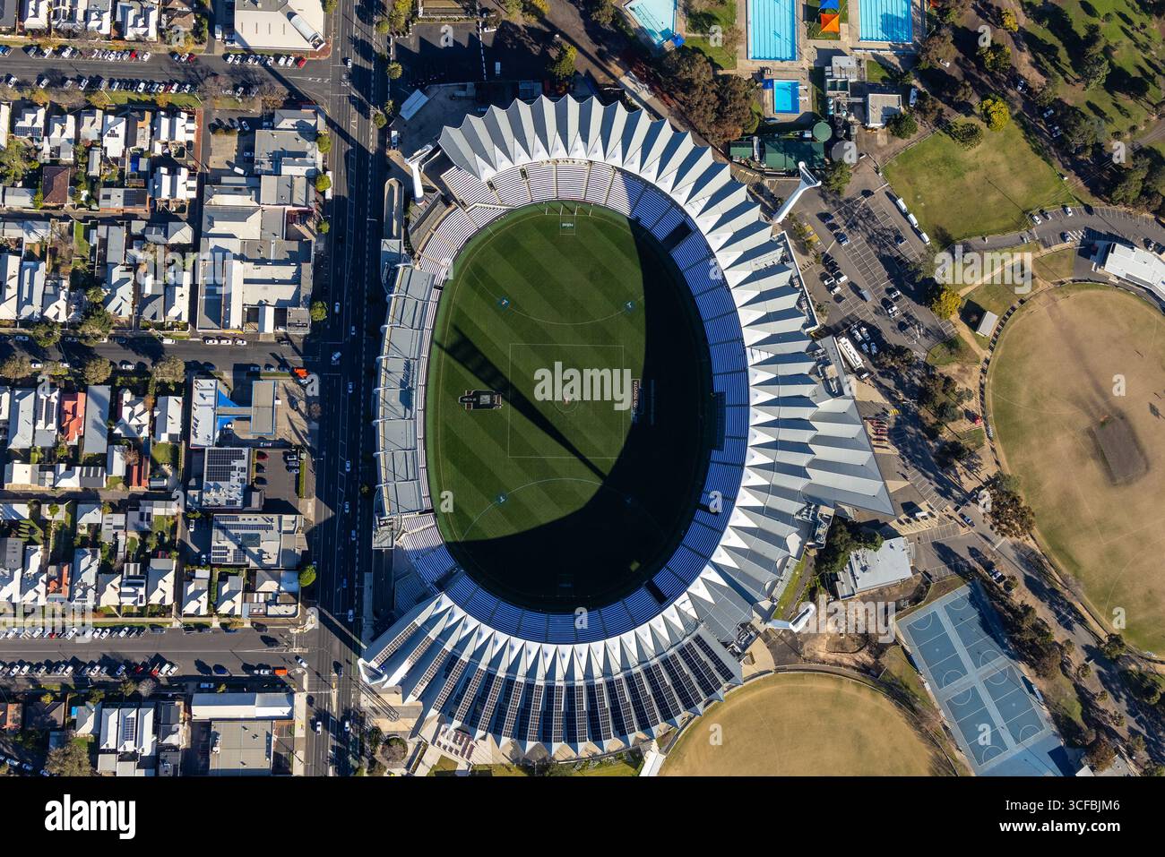 Vista aerea dell'iconico stadio Kardinia Park, circondato da strade suburbane e vegetazione lussureggiante, che getta un'ombra spettacolare sul verde vibrante Foto Stock