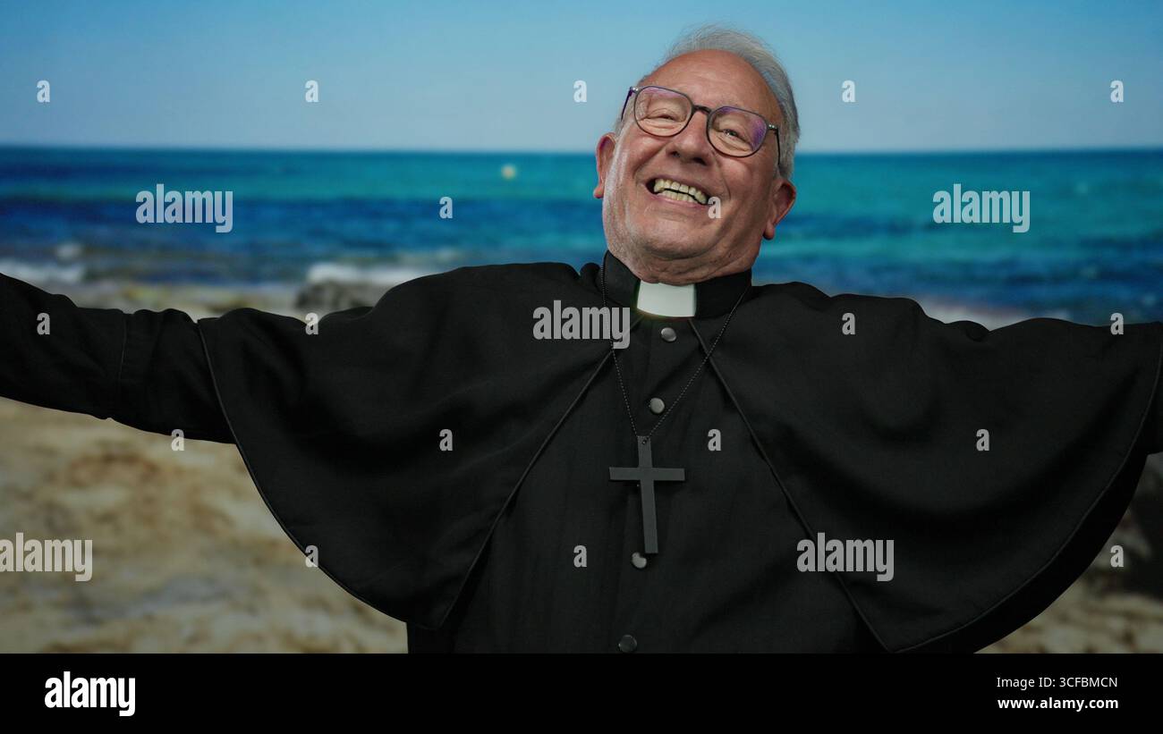 Sacerdote anziano che si gode un momento di gioia al mare con l'acqua azzurra sullo sfondo, indossando occhiali e una croce, incarnando un senso di pace Foto Stock