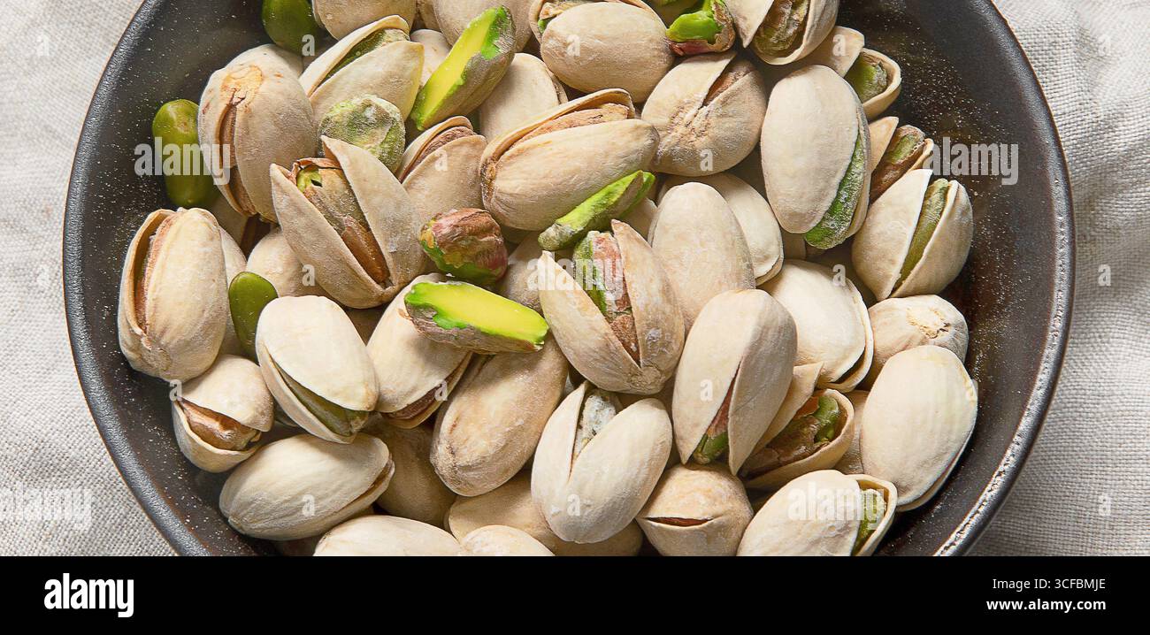 Pistacchi salati in una ciotola scura. Proteina vegetariana sana cibo nutriente. Spuntini di noci naturali. Panorama, banner Foto Stock