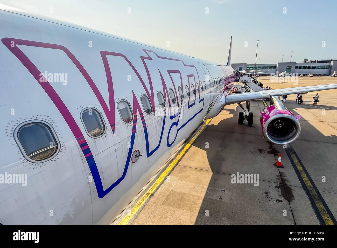 Londra, Regno Unito. 6 agosto 2025. Un aereo della Wizz Air aspetta sul pad accanto all'edificio del termianl mentre carica i passeggeri a bordo - i viaggiatori passano attraverso l'aeroporto di Luton, Luton. Crediti: Guy Bell/Alamy Live News Foto Stock