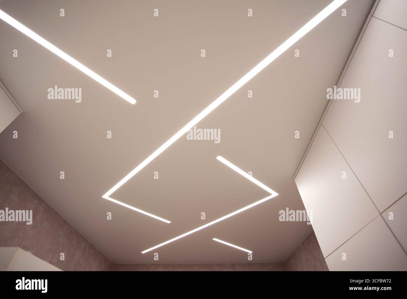 Soffitto allungato di design moderno con linee LED illuminate in camera. Foto Stock